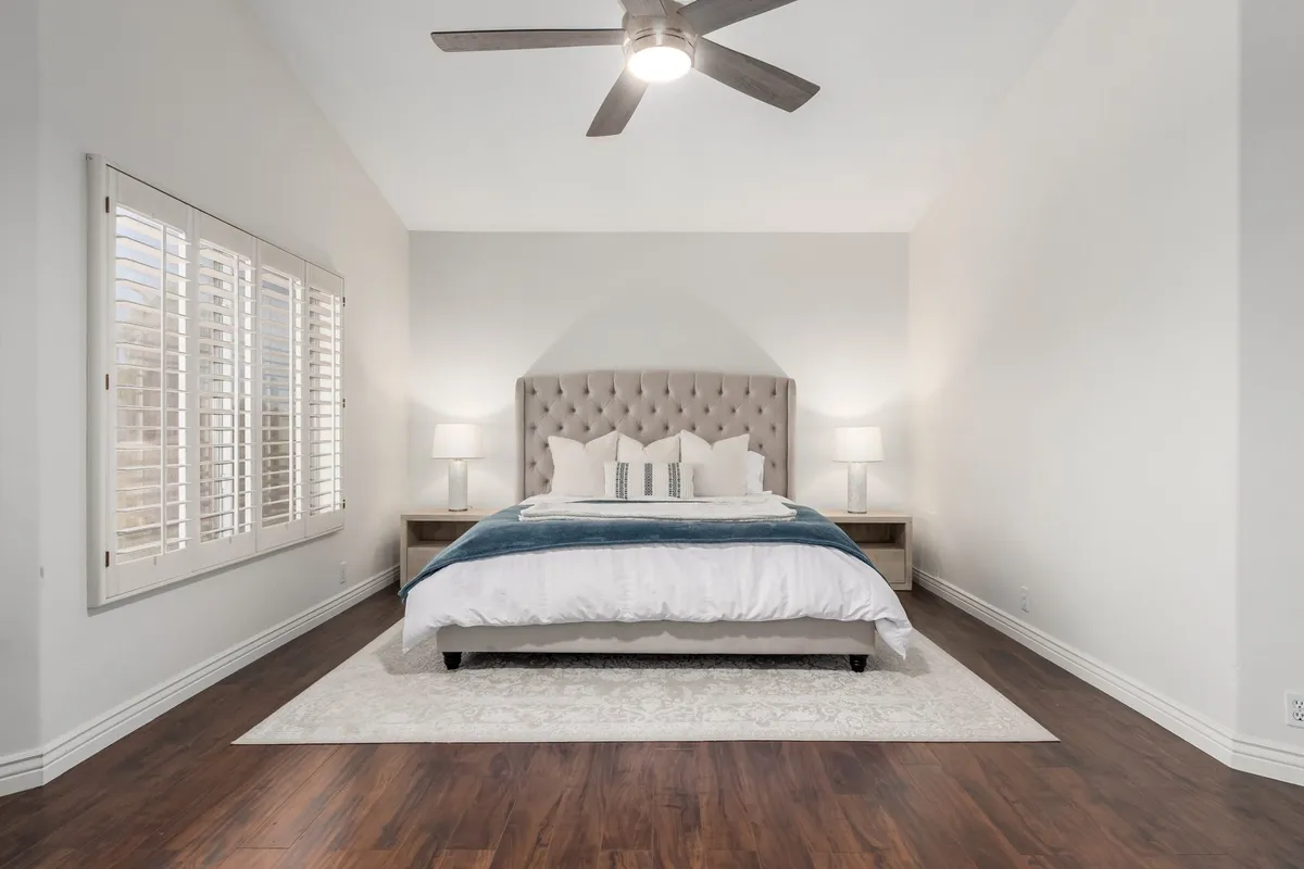 A cozy bedroom with a tufted headboard, decorative pillows, nightstands with lamps, and a soft area rug. Natural light streams in, adding to the tranquil environment, perfect for unwinding after a busy day.