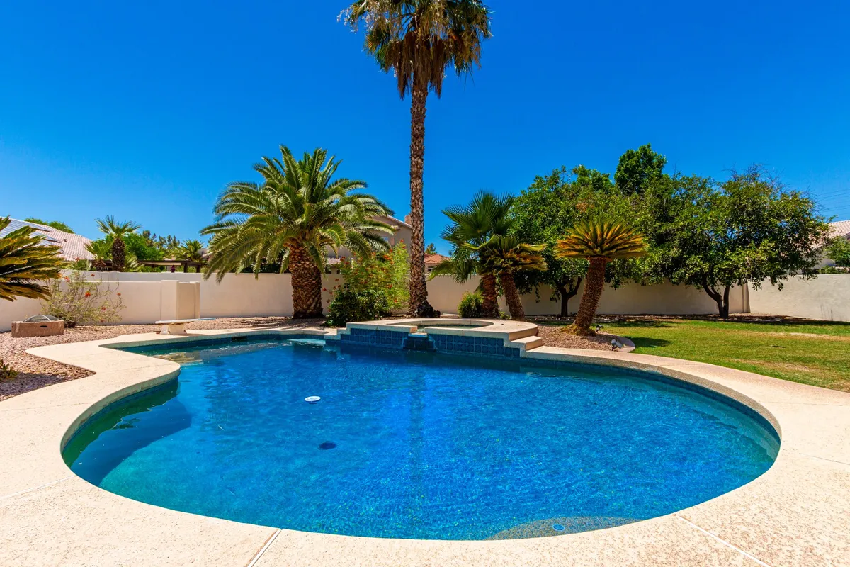 This exterior image features a sparkling swimming pool surrounded by palm trees and a landscaped garden, creating a resort-style oasis. The scene evokes leisure and relaxation, with ample space for sunbathing and outdoor gatherings.