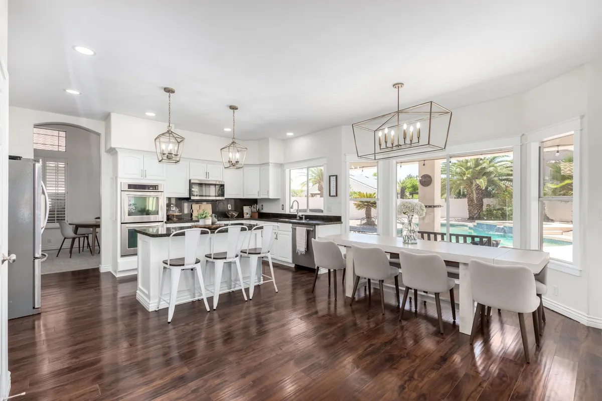 A modern kitchen with a prominent island, dining table, and expansive windows overlooking the pool, blending indoor culinary space with relaxing pool views. The scene is set for both entertaining guests and sharing daily meals in comfort and style.