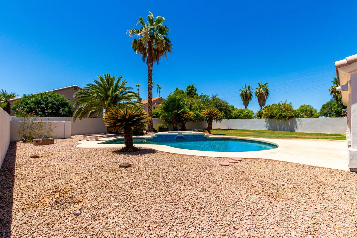 A sparkling swimming pool surrounded by mature palm trees and manicured landscaping. The pool area is designed for both relaxation and gatherings, with enough open space to lounge or host pool parties. The warm desert sky hints at a resort-like atmosphere, especially around sunset.