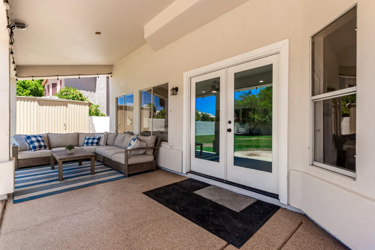 This image features an inviting outdoor seating area set atop a striped rug, with double doors that connect seamlessly to the interior. The space is ideal for gathering with friends and family, dining outdoors, or simply relaxing while enjoying the fresh air. The overall mood is casual and comfortable, evoking leisurely afternoons or cozy evenings outside.