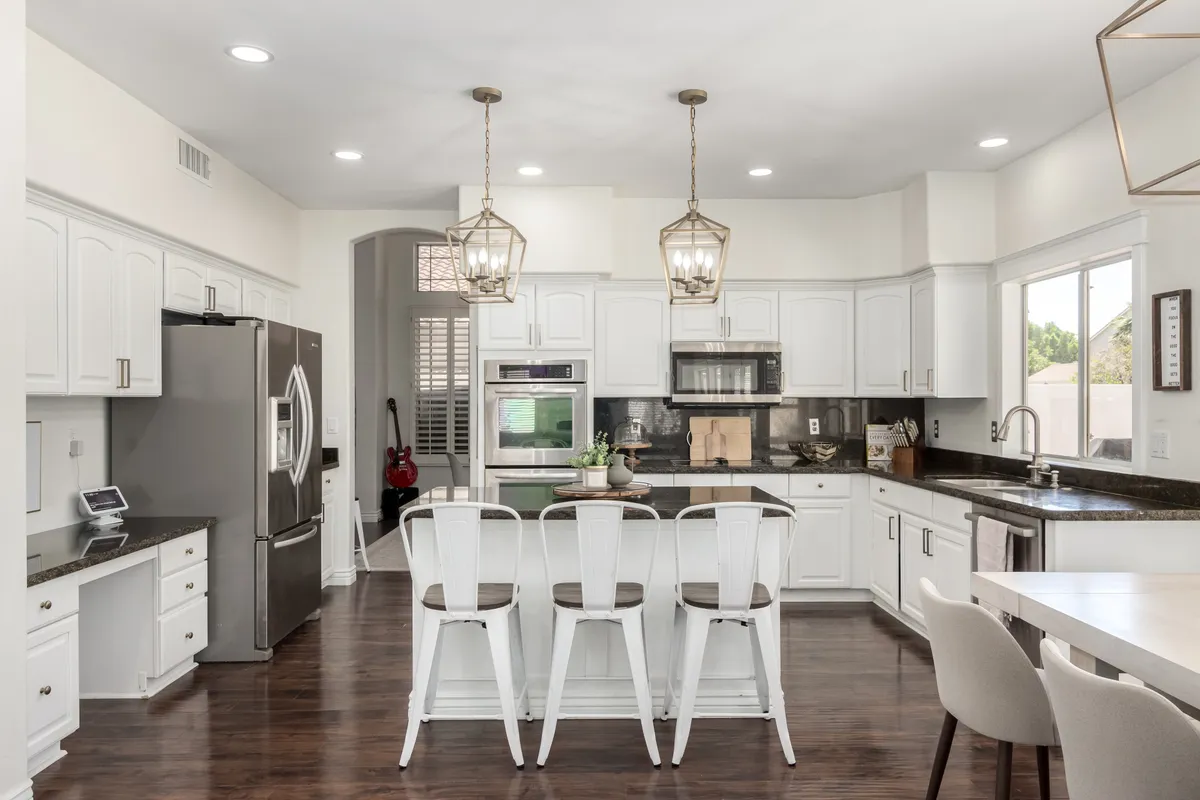 A bright, modern kitchen featuring a spacious island with bar stools, overhead pendant lights, sleek granite countertops, and state-of-the-art appliances. The open layout allows for easy movement and interaction, encouraging both cooking and socializing.