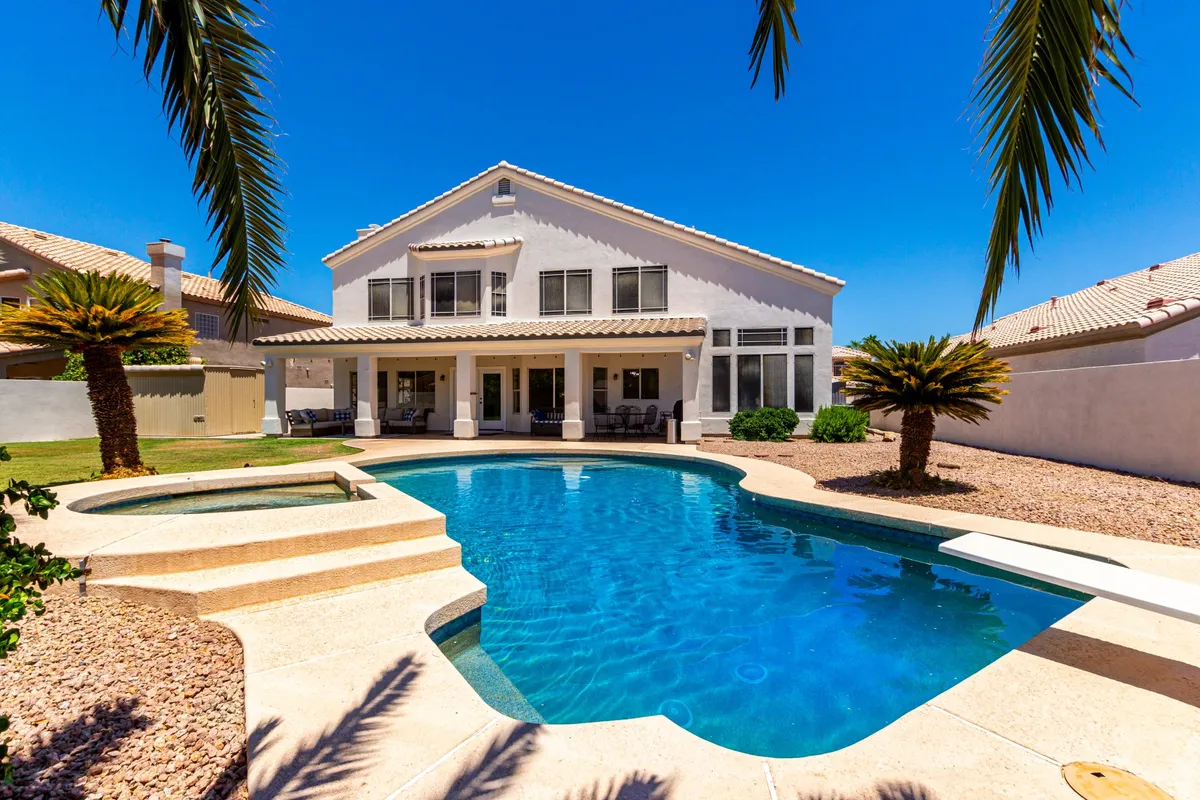An elegant exterior shot showcasing a sparkling swimming pool bordered by palm trees and an outdoor seating area. The house façade is visible, suggesting an inviting environment for swimming, sunbathing, or alfresco dining. The setting is serene and refreshing, ideal for celebrating with friends or unwinding after a fun day at nearby parks.