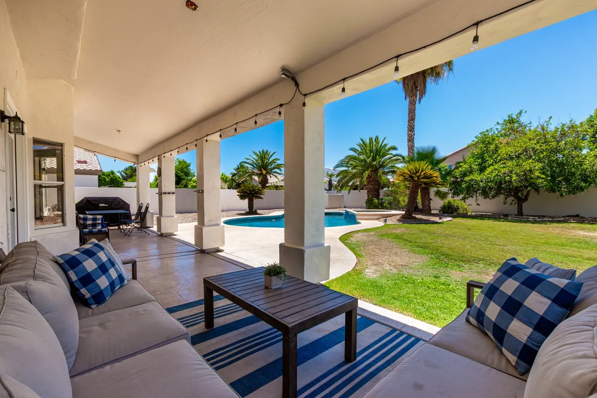 This image features an inviting outdoor seating area adjacent to a sparkling swimming pool, bordered by lush palm trees. The space is set for entertaining, with comfortable chairs and a backdrop that transitions from playful sunlit mornings to cozy, sunset evenings.
