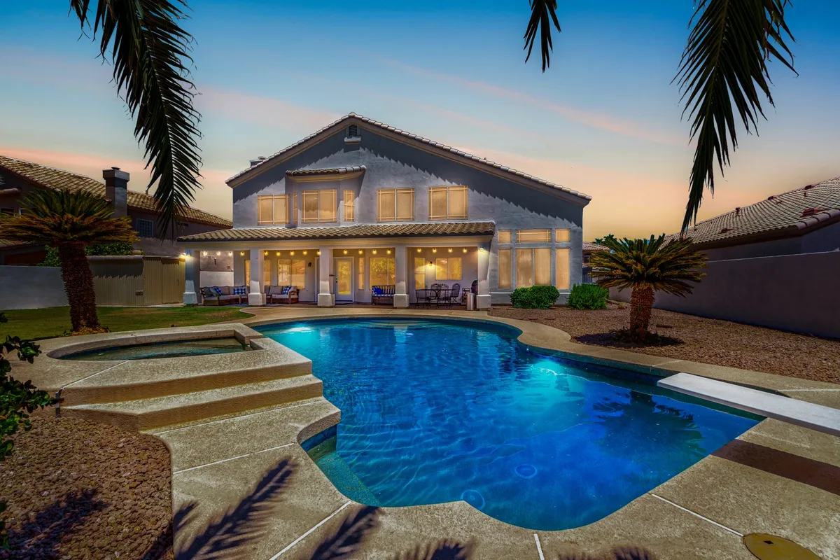 The hero image displays a sunlit backyard oasis featuring a sparkling swimming pool surrounded by palm trees, a spacious patio ideal for outdoor dining and relaxation, and the inviting facade of a stylish single-family home. The setting exudes warmth and comfort, perfect for gatherings and leisurely moments under the Arizona sky.