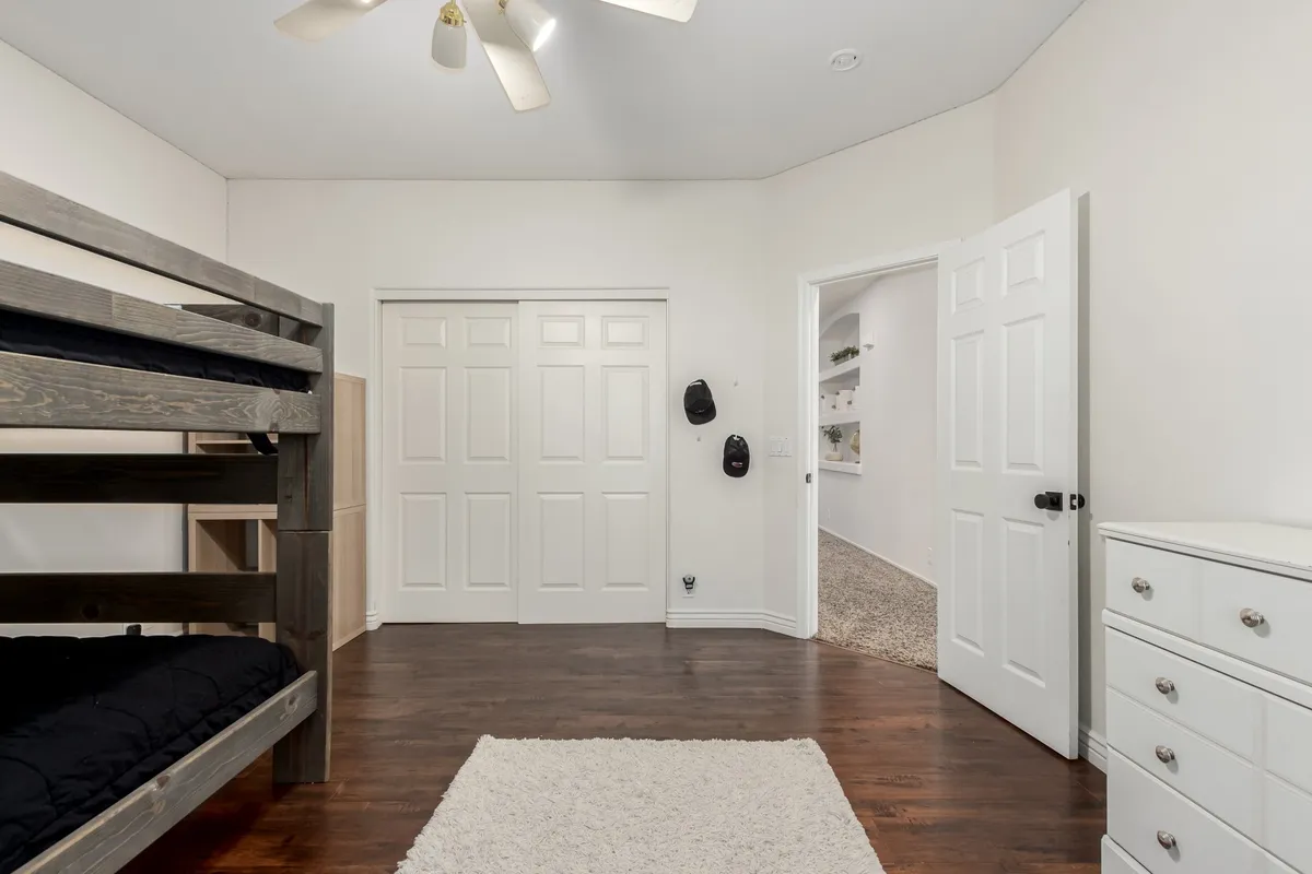 A cheerful and relaxed bedroom with a bunk bed, white dresser, light-colored rug, and closed double doors. The space is tailored for children or groups, emphasizing both comfort and playful coziness.