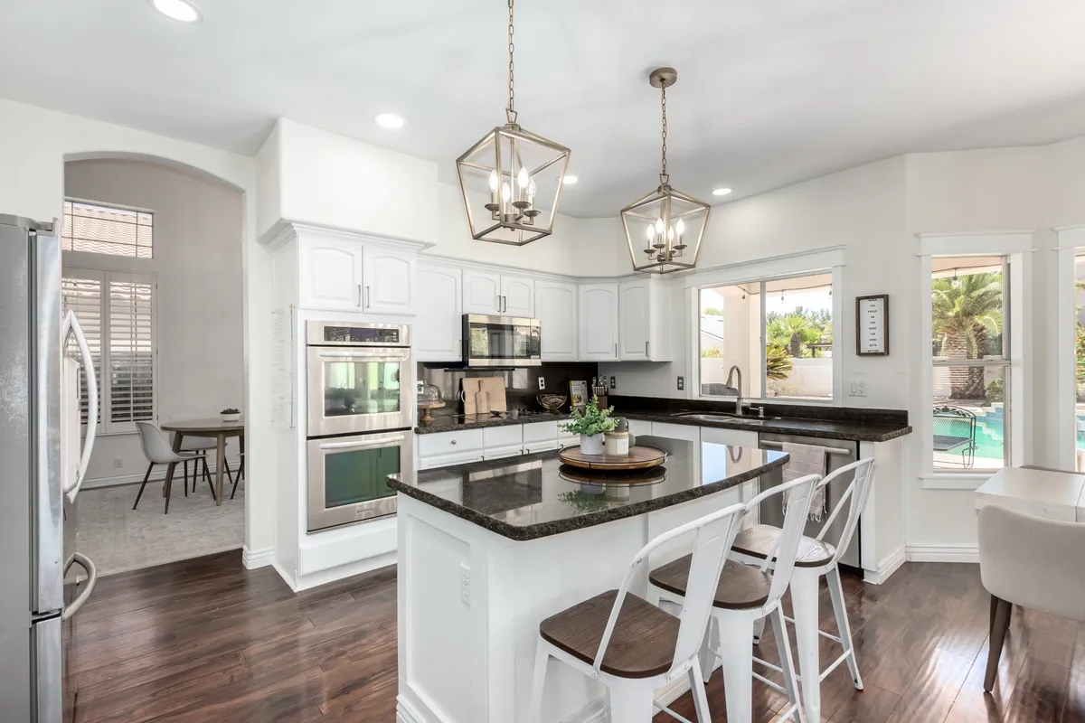 This image features a spacious, modern kitchen with granite countertops, contemporary appliances, and large windows that overlook the pool area. The kitchen is open and seamlessly blends into the adjacent family gathering spaces, making it ideal for both meal preparation and socializing. The inviting lighting and visual connection to the outdoors create a sense of flow between indoor and outdoor living.